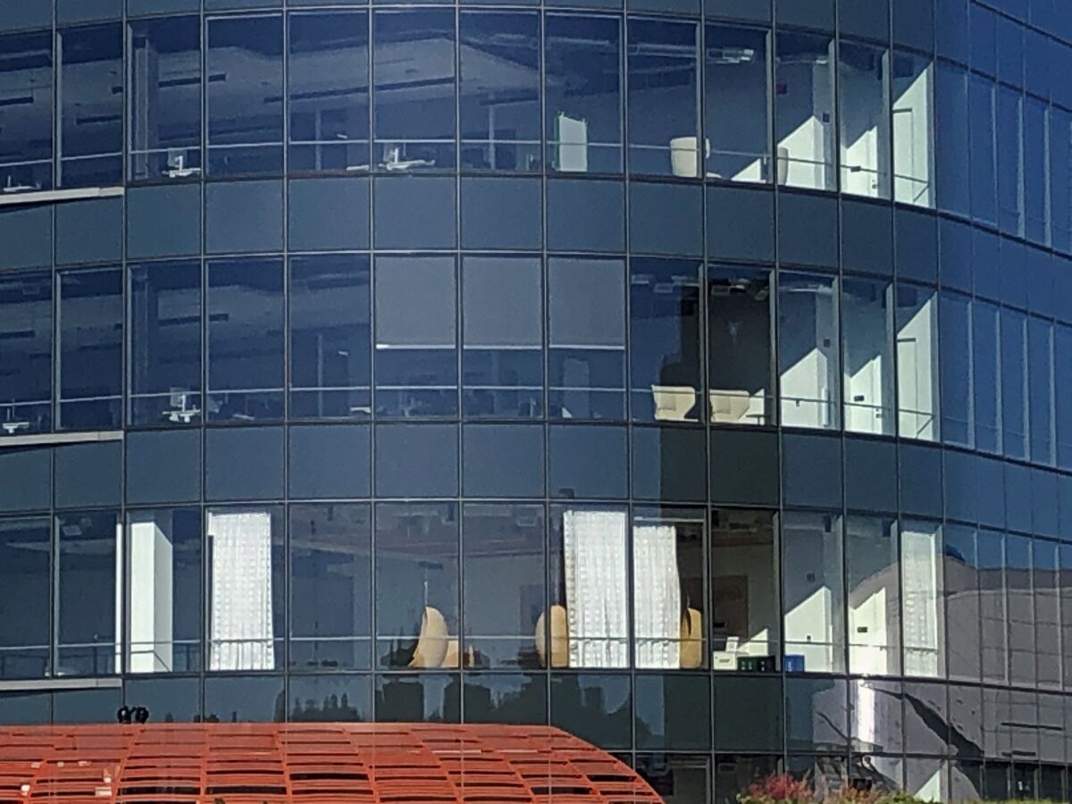 A window in a glass office tower reveals rattan egg chairs hanging from the ceiling of a partially curtained room.