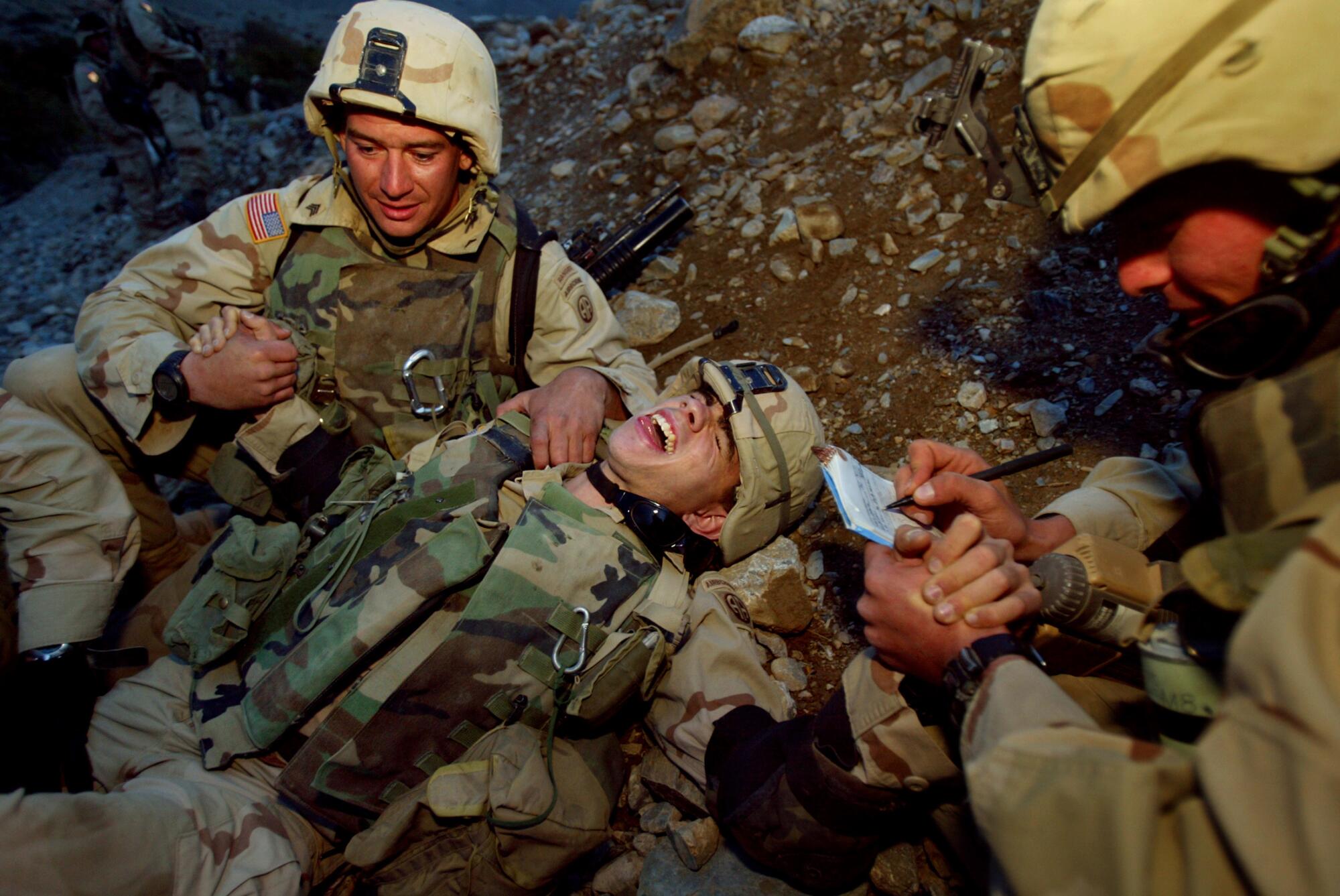 A soldier lies on the ground yelling as other soldiers tend to him