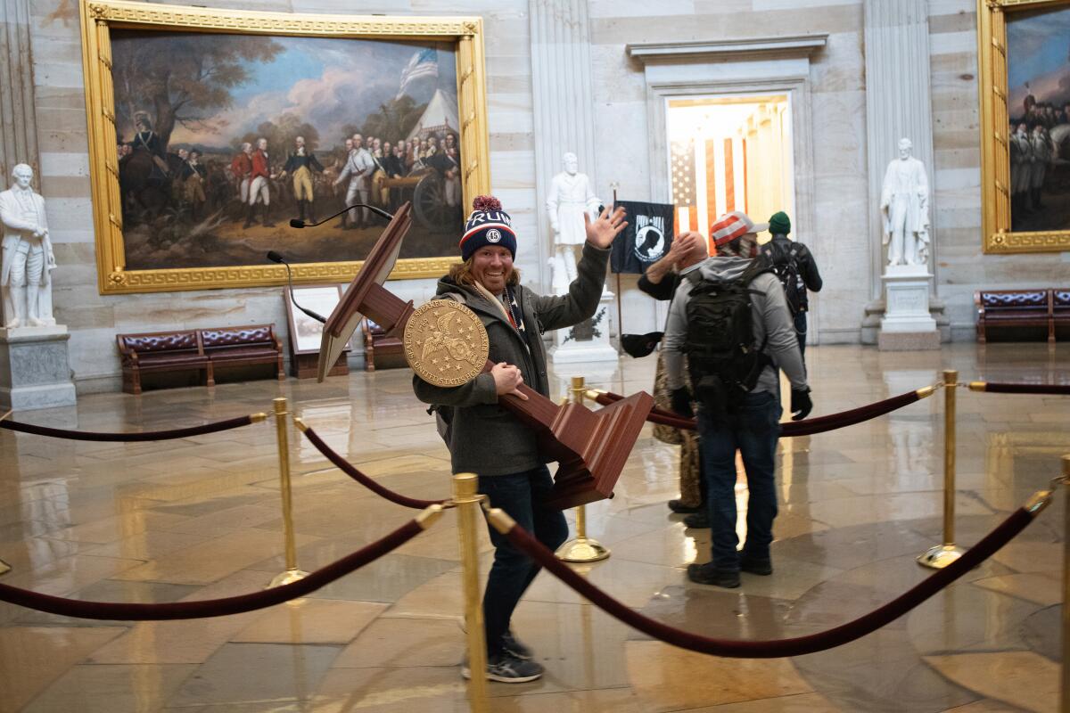 A pro-Trump extremist in a ski hat waves at a camera as he carries the house speaker's lectern through the Capitol's rotunda.