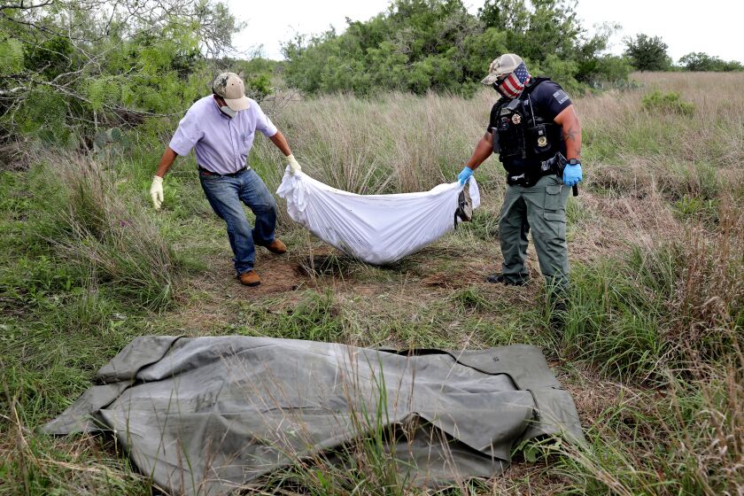 FALFURRIAS, TEXAS - JUNE 04: Alonzo Rangel, left, funeral director of Funeraria (cq) Del Angel, and Brooks County Deputy Raul Narvaez, 31, after an inspection, remove the remains of deceased female migrant, Rosario Yanira Giron de Orellana, 40, of El Salvador, found on a ranch in Brooks County on Friday, June 4, 2021 in Falfurrias, Texas. Rosario's body was transported to the Brooks County Sheriff's office portable morgue. Increased numbers of adult migrants crossing the border illegally, avoiding U.S. Border Patrol, Rio Grande Valley Sector, by walking around check points and dying in the brush. (Gary Coronado / Los Angeles Times)