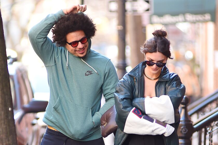 A man with an afro in a green hoodie walking alongside a woman in a black leather jacket and her hair in a bun