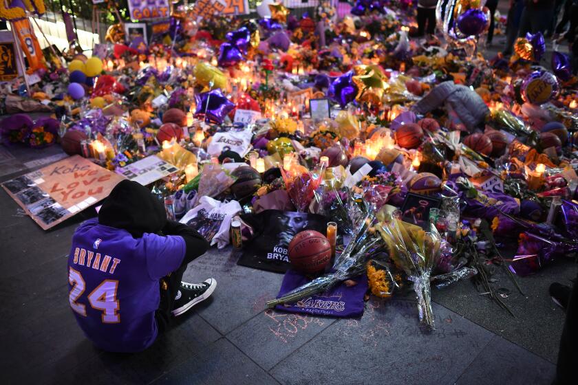 LOS ANGELES, CALIFORNIA JANUARY 28, 2020-A fan sits alone at a make-shift memorial at L.A. Live in Downtown Los Angeles after the death of Lakers star Kobe Bryant. (Wally Skalij/Los Angeles Times)