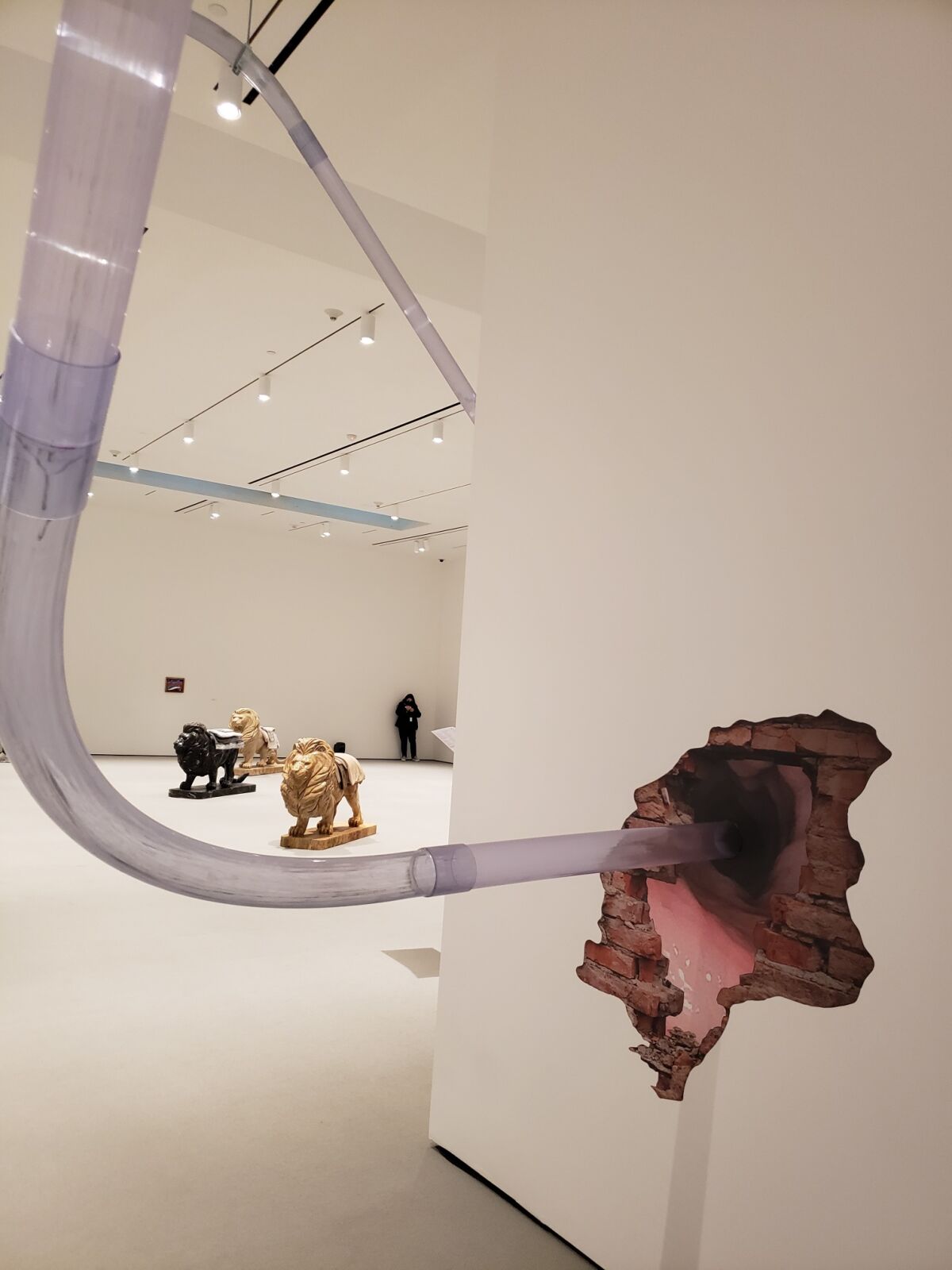 A tube leading into a wall with an image of a hole, with three lion scultptures in the background
