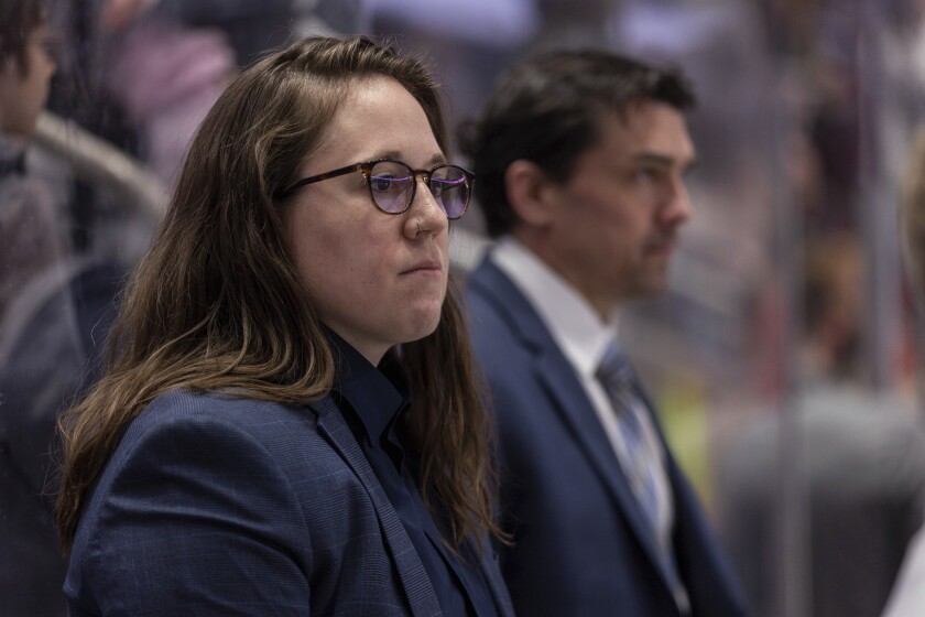 Emily Engel-Natzke stands on the bench in front of associate goaltending coach Alex Westlund during pregame warmups before the Hershey Bears played the Springfield Thunderbirds in an American Hockey League game on Sunday, April 10, 2022, in Hershey, Pa. Engel-Natzke was promoted from Hershey to video coach of the Washington Capitals on Thursday, June 30, 2022, making her the first woman to hold that position in the National Hockey League. (Photo courtesy of the Hershey Bears via AP)