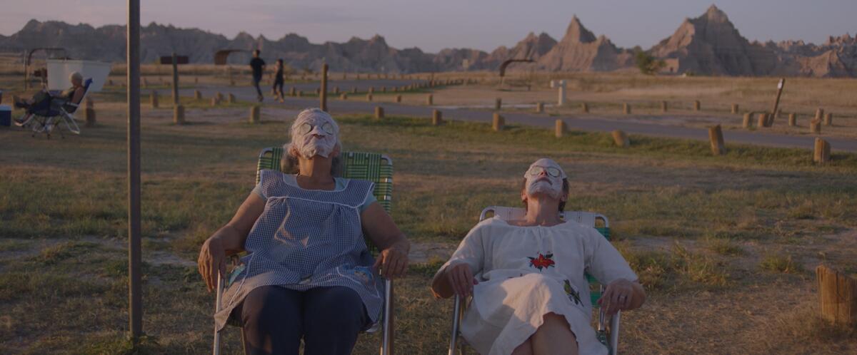 Linda May and Frances McDormand, with facial masks, sit outside in "Nomadland."