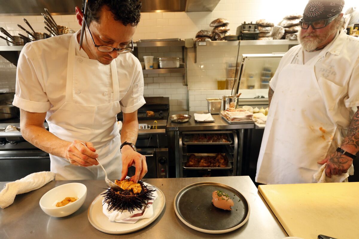 Chef Jesse Barber, left, places uni on a bed of black risotto served inside a hollowed shell of a sea urchin.