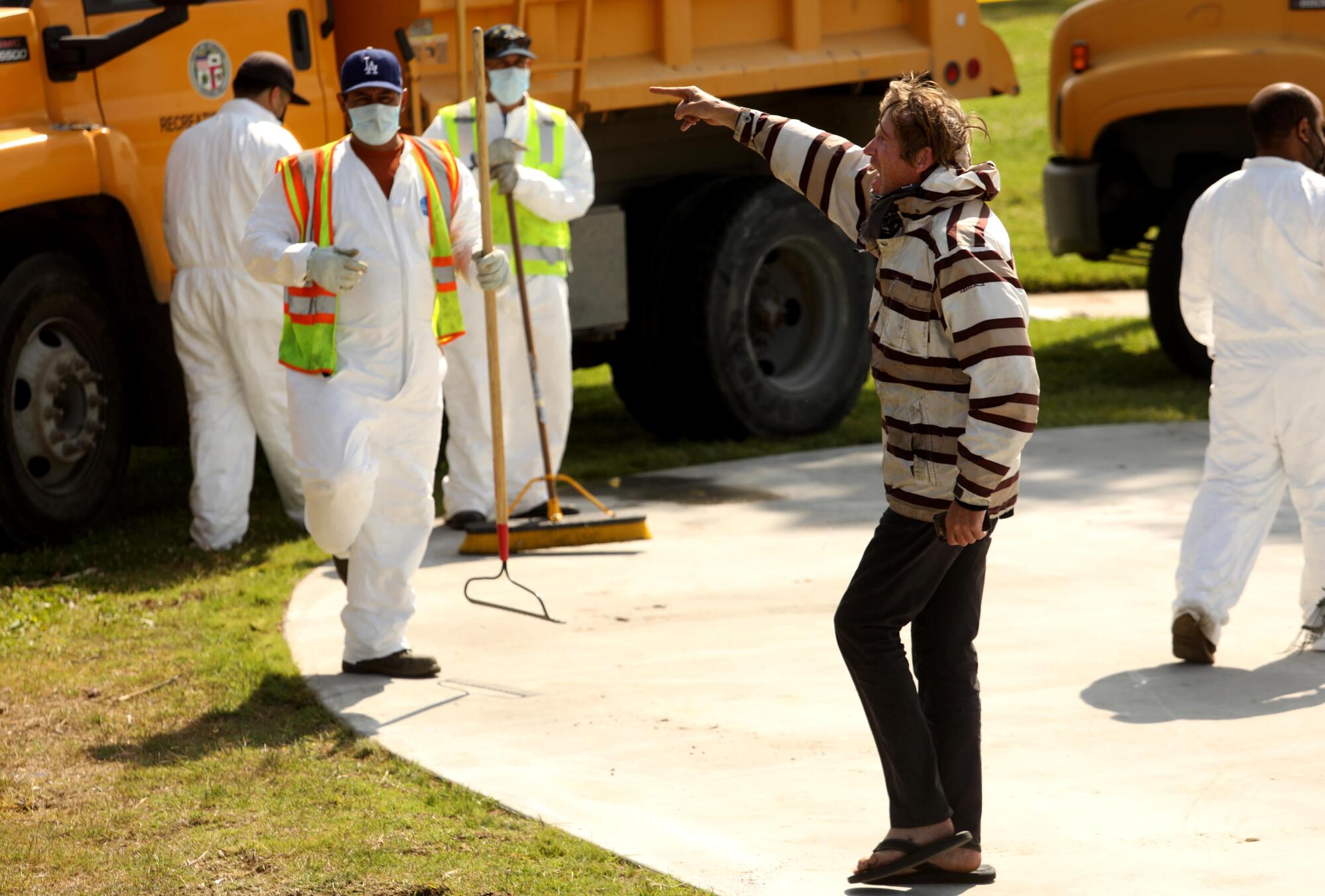 A homeless man yells at a sanitation crew workers in white jumpsuits
