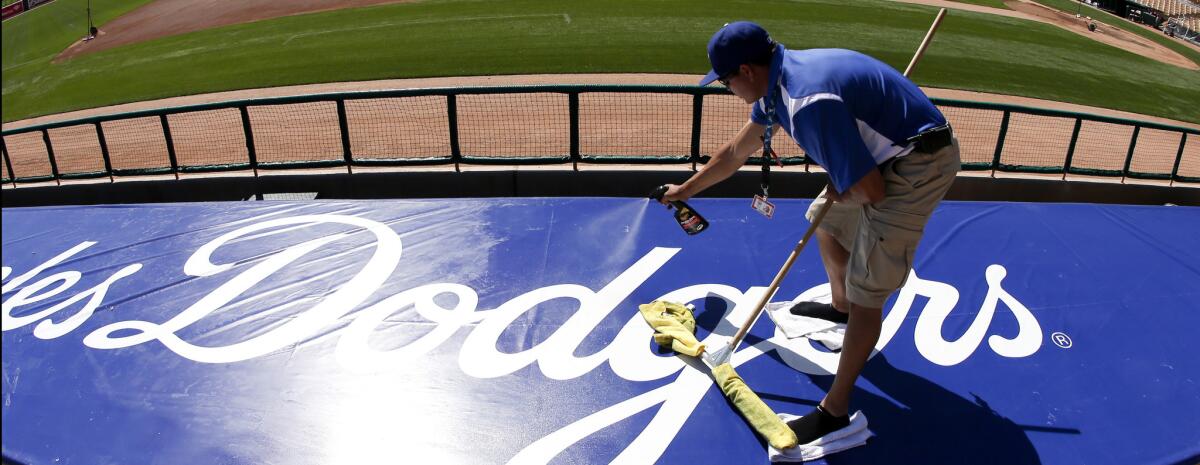 Jose Acuna cleans the Los Angeles Dodgers logo on top of the dugout before a spring training baseball game against the Milwaukee Brewers in Glendale, Ariz., on Sunday, March 8, 2015. (AP Photo/Chris Carlson)