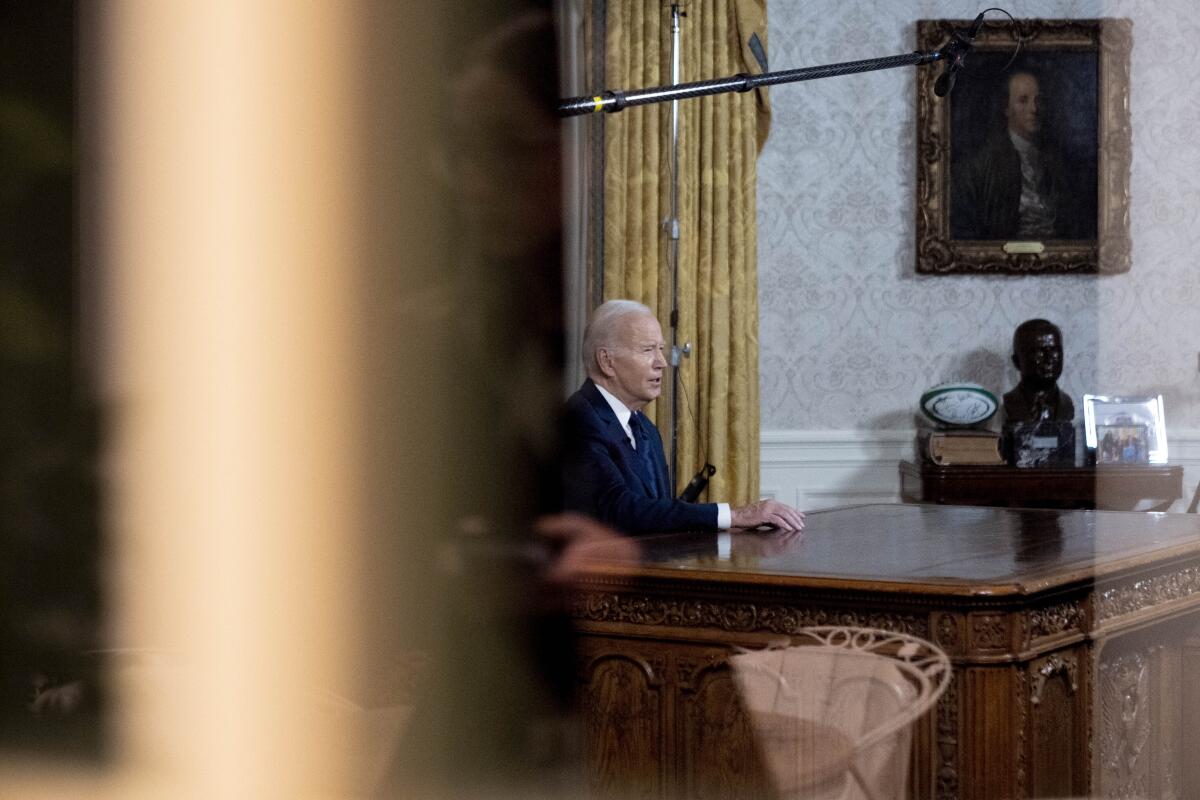 Biden seated at the Resolute Desk of the Oval Office speaking into a camera, out of frame