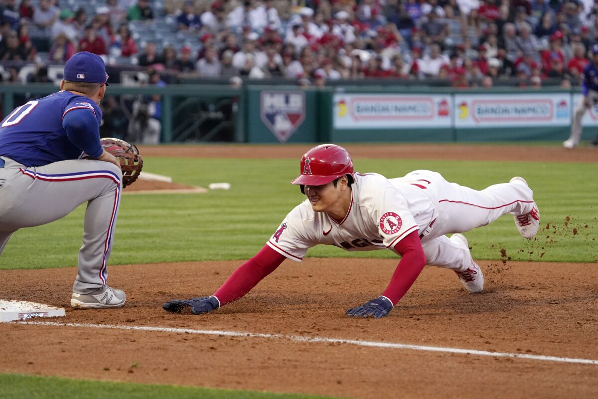 Angels' Shohei Ohtani dives back to first safely as Texas Rangers' Nathaniel Lowe takes the throw from the mound.