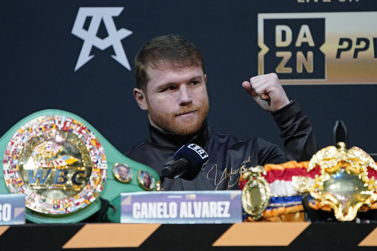 Canelo Álvarez raises his fist while sitting in front of his title belts during a news conference 