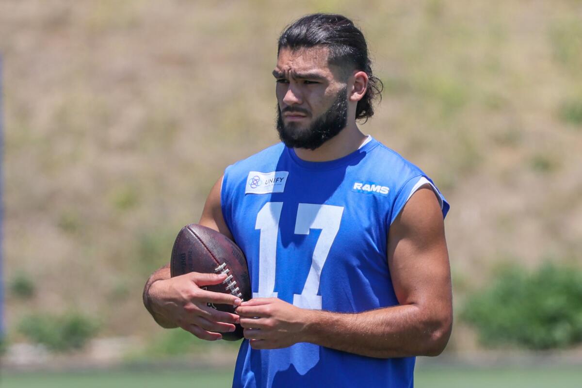  Rams receiver Puka Nacua holds a football on the sideline during practice.