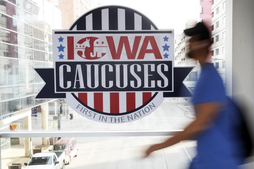 FILE - A pedestrian walks past a sign for the Iowa Caucuses on a downtown skywalk, in Des Moines, Iowa, on Feb. 4, 2020. Iowa’s Democratic Party says it will hold a caucus on Jan. 15 but won’t release the results until early March. It's an attempt to retain their state’s leadoff spot on the presidential nominating calendar without violating a new national party lineup endorsed by President Joe Biden that has South Carolina going first for 2024. (AP Photo/Charlie Neibergall, File)