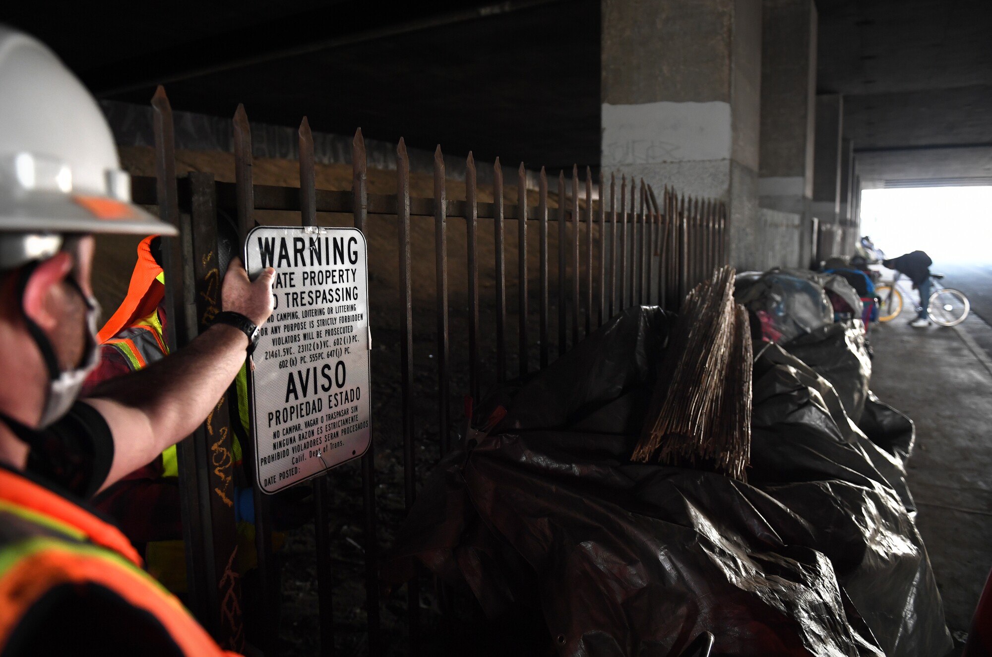 Crews post signs next to a homeless encampment under the 405 Freeway in Inglewood.
