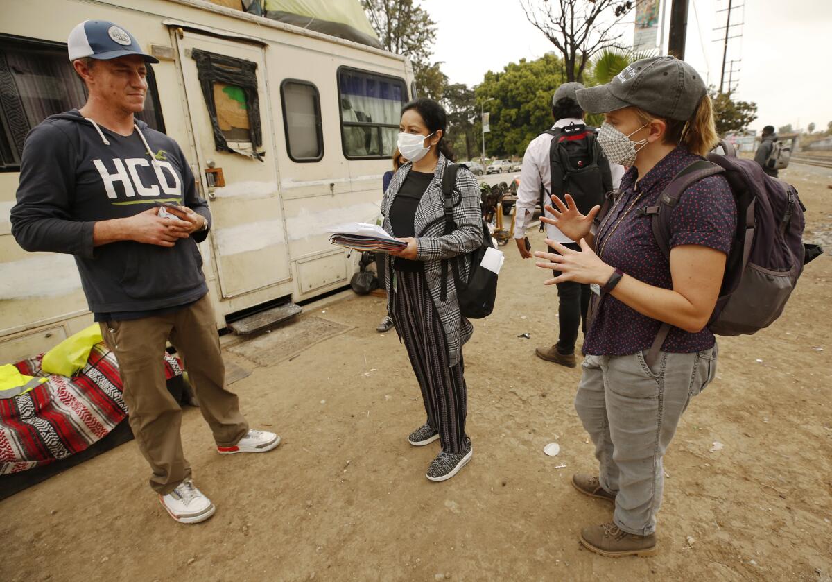 Two women in masks talk to an unmasked man outside an RV.