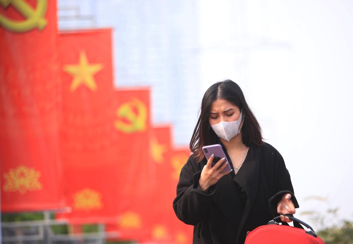 A woman wearing a face mask looks at her phone in Hanoi.