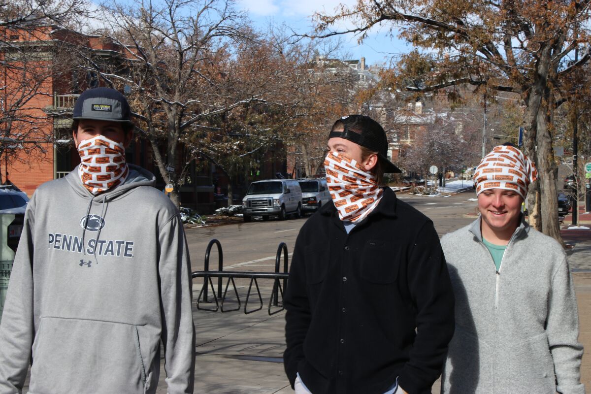 Two men wear masks and a third, smiling, wears his mask on his head in in Boulder, Colo.