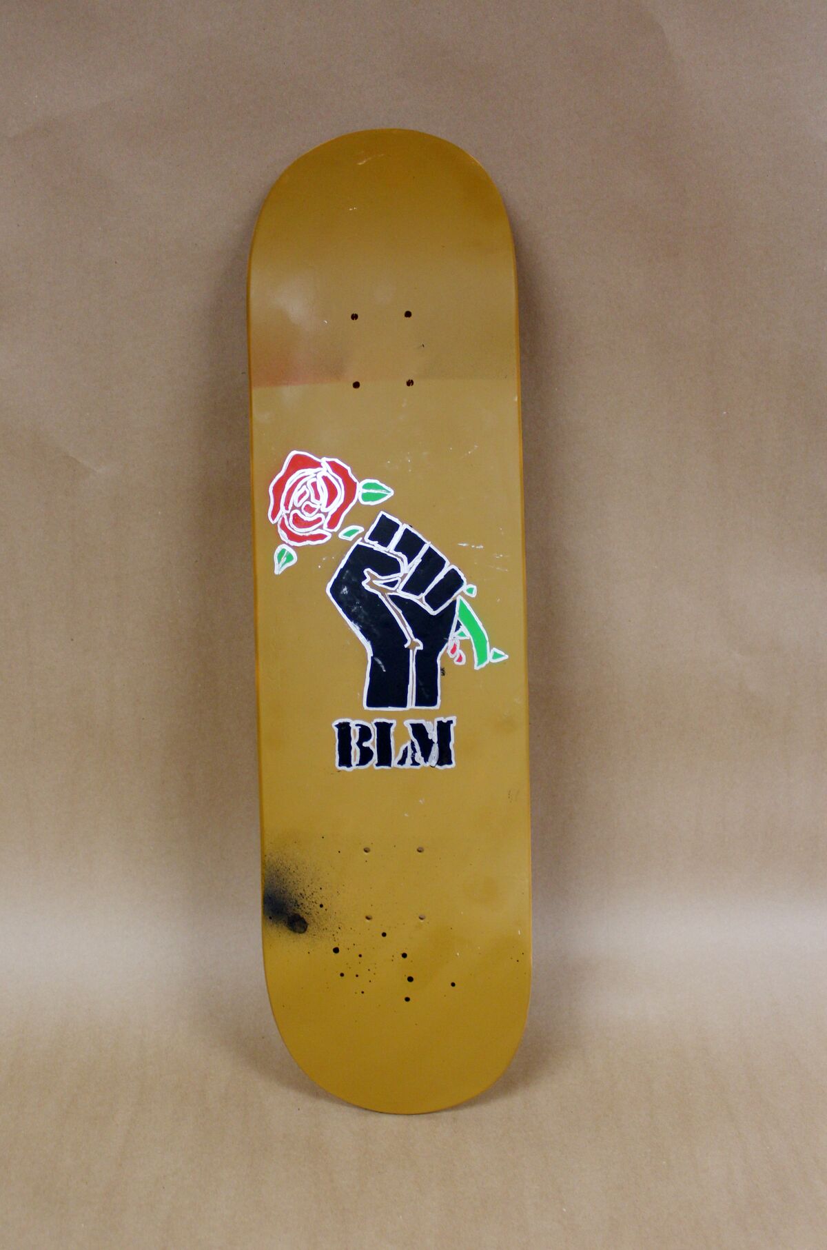 A skateboard with a clenched, raised fist holding a red rose above the letters BLM.