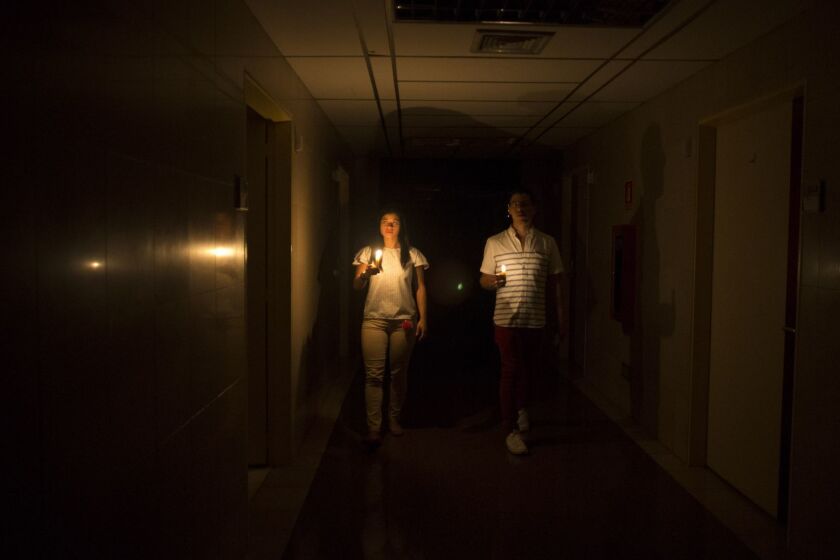Relatives of a patient walk in the darkened hall of a clinic with a candle lighting the way, during a power outage in Caracas, Venezuela, Thursday, March 7, 2019. A power outage left much of Venezuela in the dark early Thursday evening in what appeared to be one of the largest blackouts yet in a country where power failures have become increasingly common. (AP Photo/Ariana Cubillos)
