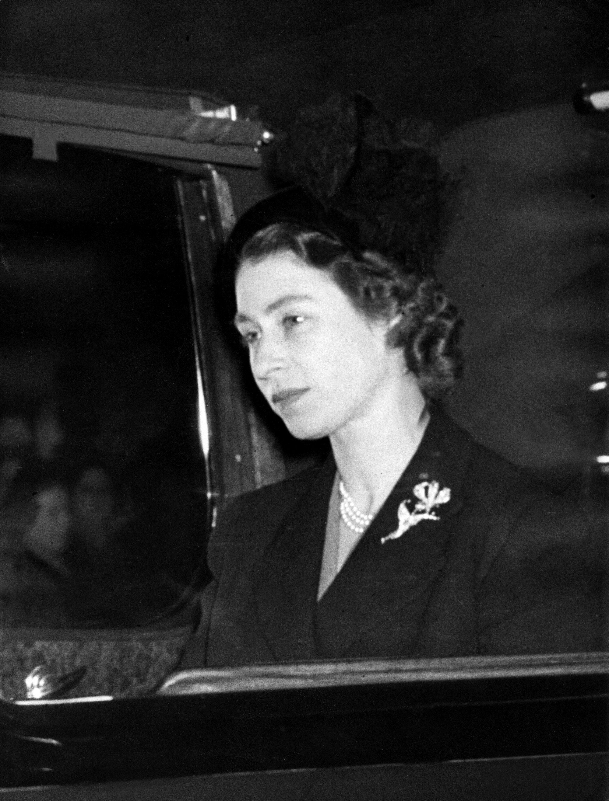 A woman in a dark hat and suit is seen in a car