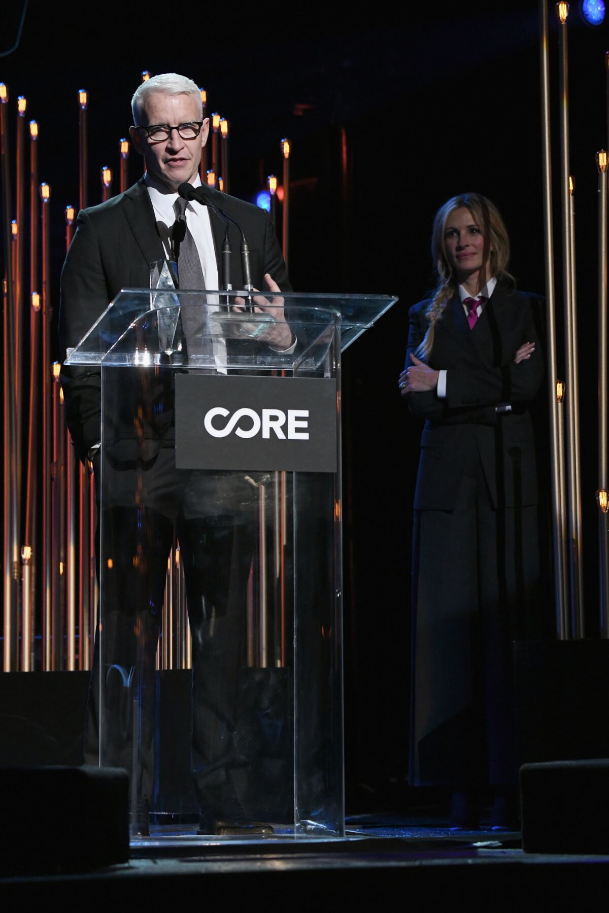 Honoree Anderson Cooper speaks onstage as Julia Roberts looks on at Sean Penn's CORE gala.