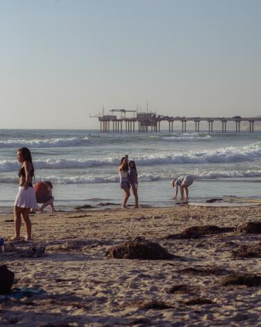 People take selfies and hang out at La Jolla Shores in San Diego, California. Photographed in June 2024.