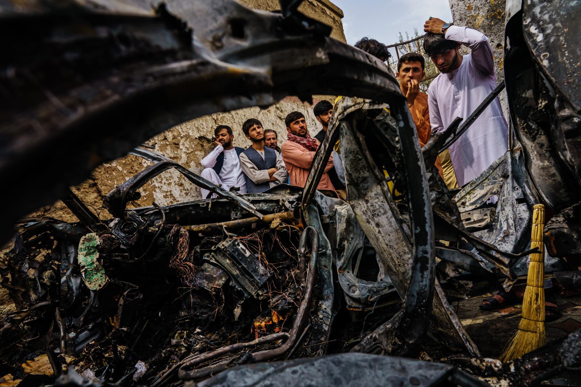 People gather near the burned remains of a vehicle 