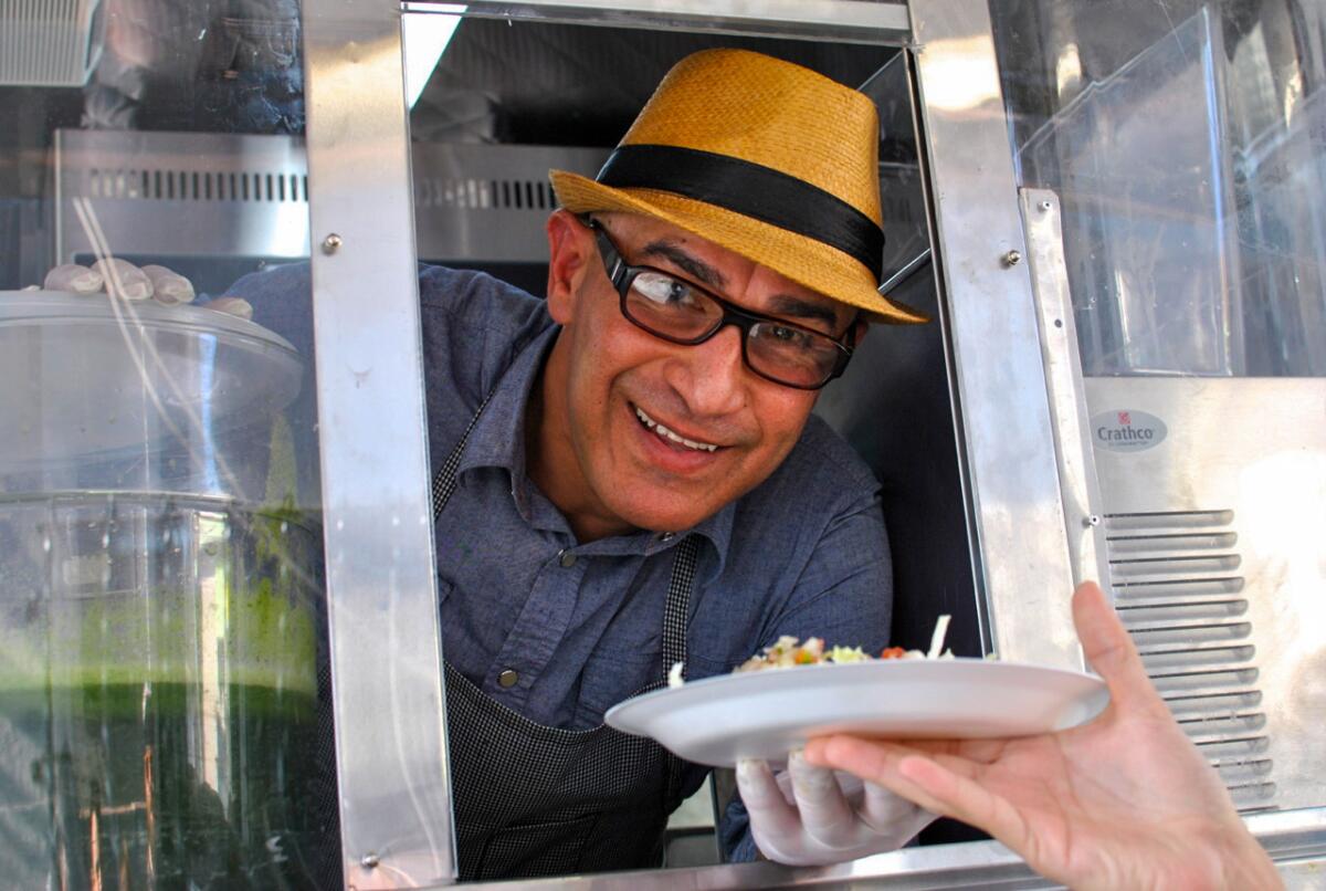 A man leans out the window of a food truck, passing a plate of tacos to an outstretched hand.