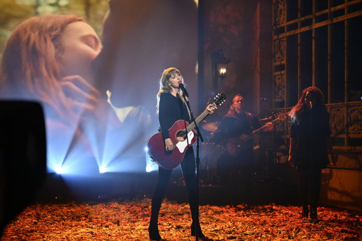 Taylor Swift plays a guitar and sings on a stage covered with autumn leaves
