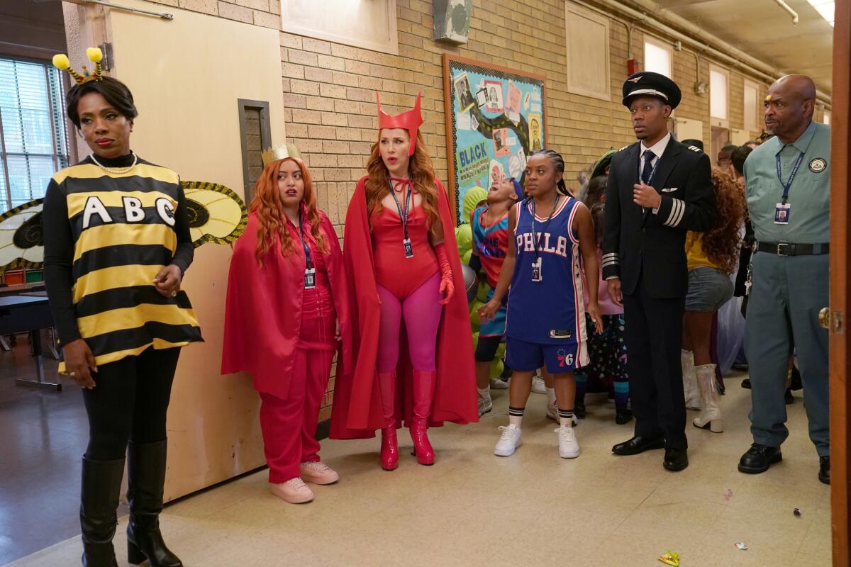A group of teachers dressed as a bee, devils, a basketball player and a pilot stand in the school hallway.
