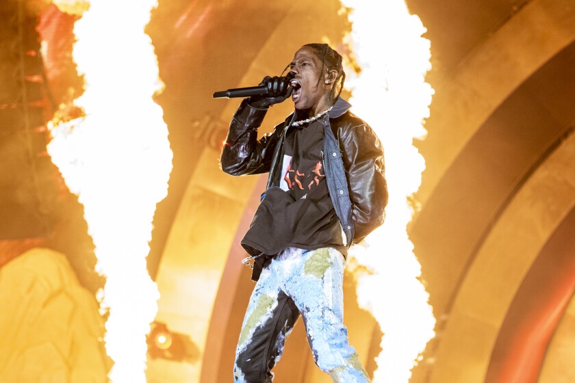 A man in a leather jacket sings into a mic with pyro effects in the background