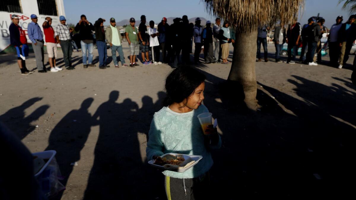 Suaniy Gomez, 9, of Honduras, with a plate of donated food, stands with other migrants Dec. 12 in front of an abandoned concert venue turned government shelter in Tijuana.