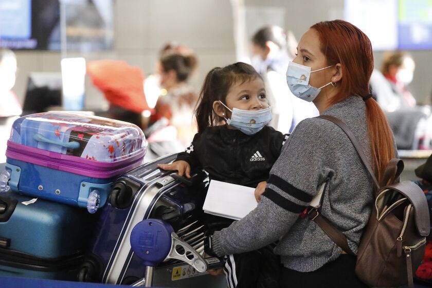 LOS ANGELES, CA - NOVEMBER 16: Passenger Karen Alvarez comforts her 3-year-old daughter Mercedez Gomez as they wait in line at the Tom Bradley International Terminal at LAX before their flight to Nicaragua on Monday November 16, 2020 as weekly coronavirus cases have doubled in just the last month around the state, and Los Angeles County had the grim distinction of recording more than 6,800 cases this weekend alone, an alarming spike that has officials talking about more restrictions. California officials are urging those who do head out of state to self-quarantine for 14 days when they return. LAX Los Angeles Airport on Monday, Nov. 16, 2020 in Los Angeles, CA. (Al Seib / Los Angeles Times