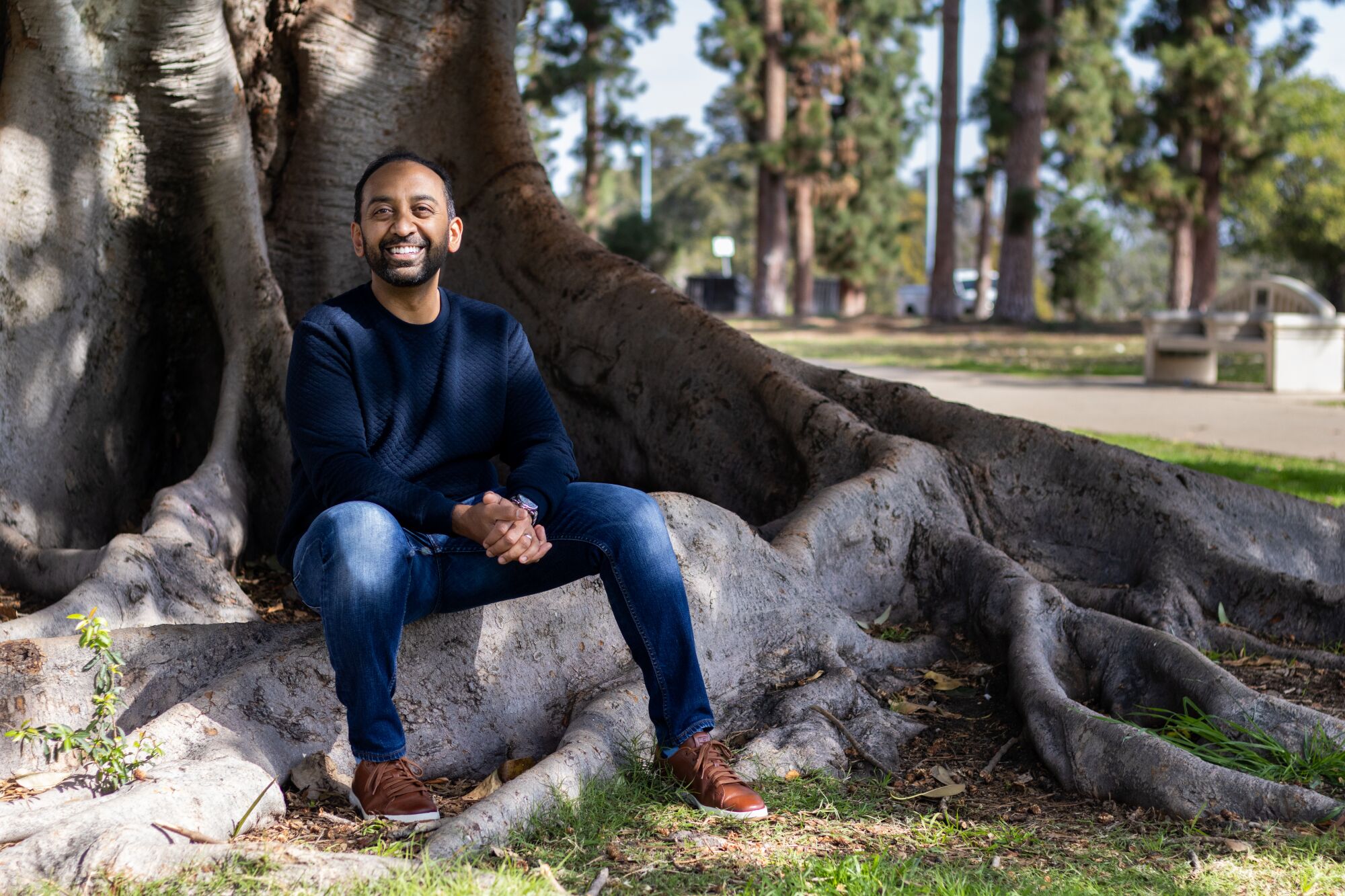 Sameer Patel photographed in Balboa Park sitting on the roots of a large banyan tree.