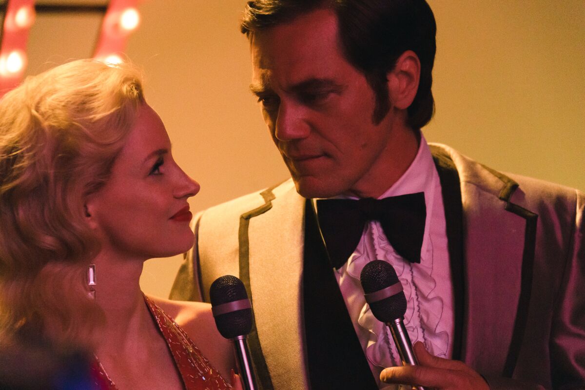 A man and woman look lovingly at each other as they stand in front of microphones in "George & Tammy."