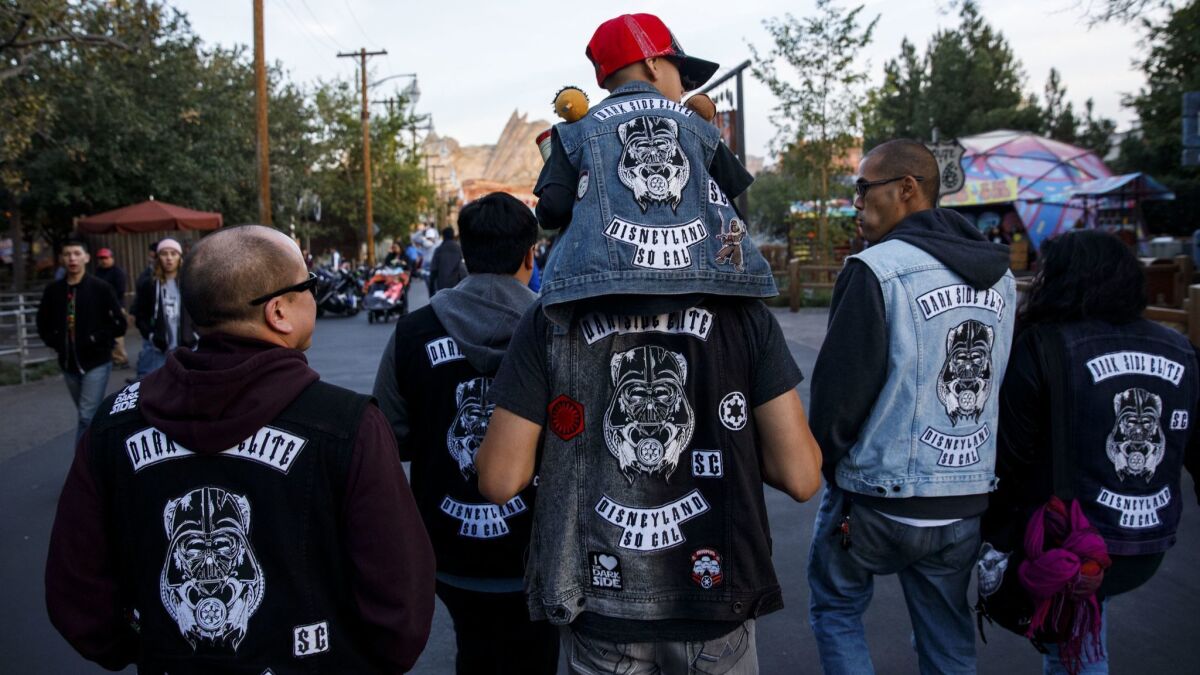 Jose Avalos carries his son Nathan, 7, on his shoulders as members of the "Dark Side Elite" social club walk to Cars Land at Disney California Adventure Park. The founders of a social club are accusing another club of intimidation and spreading false information.