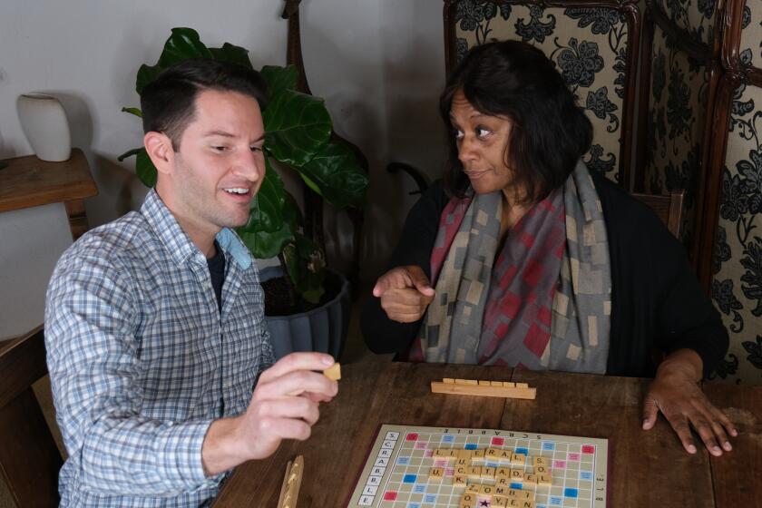 A white man and black woman play Scrabble. 