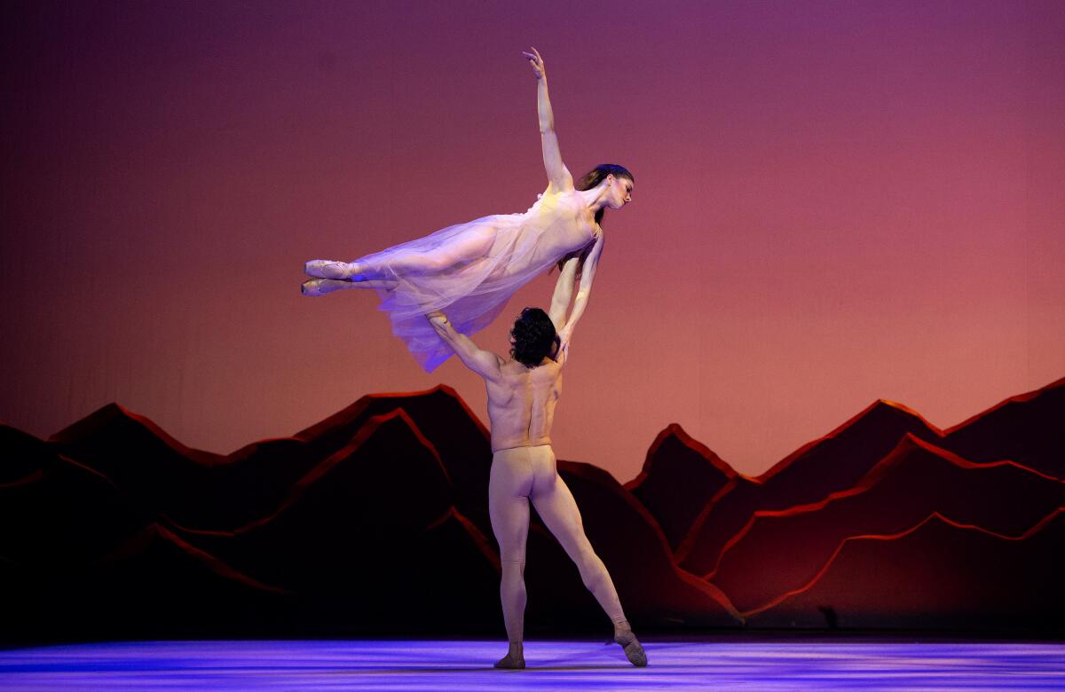 A male ballet dancer lifts a female dancer over his head.