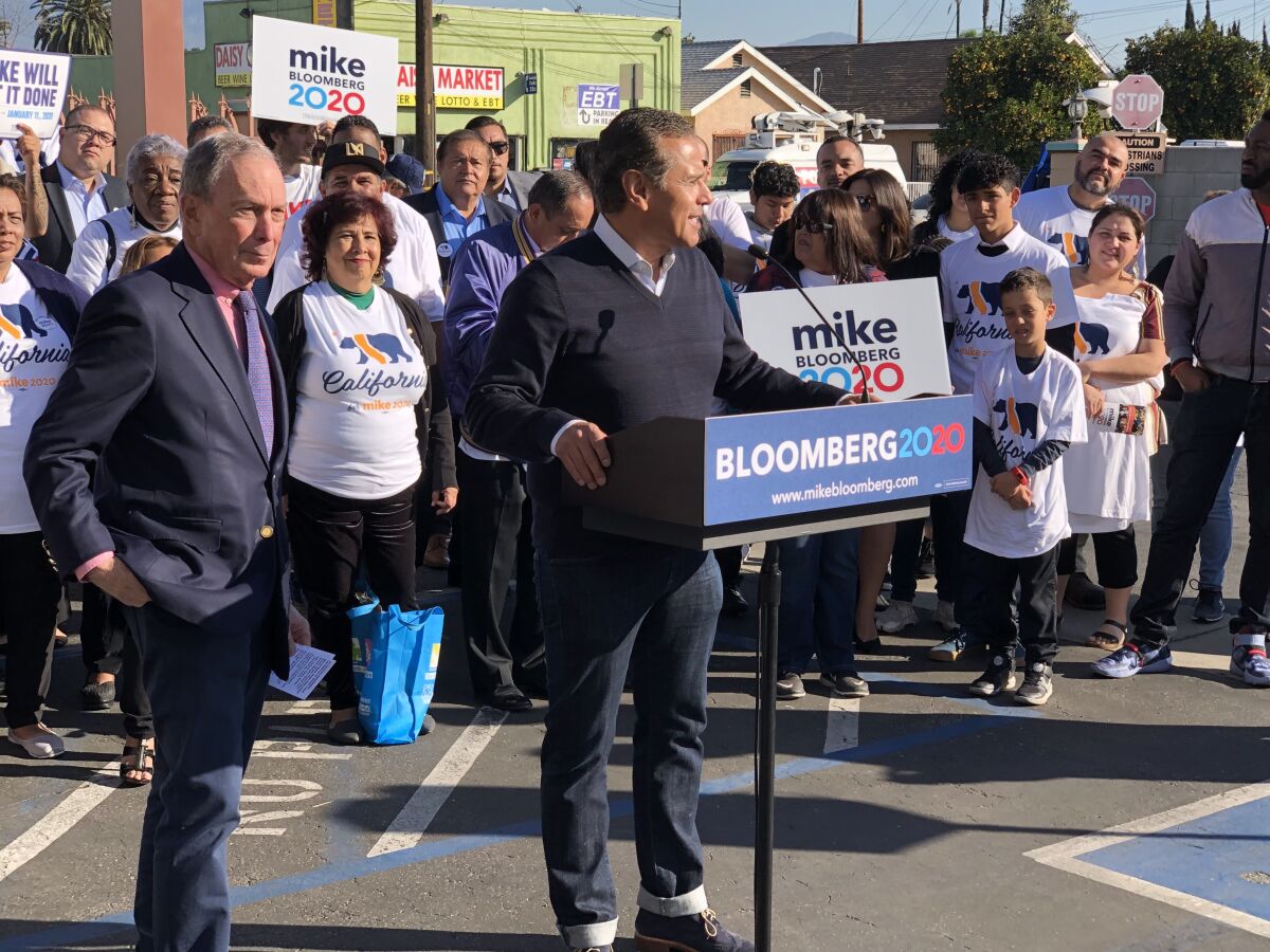 Michael Bloomberg stands to the side as Antonio Villaraigosa addresses an outdoor crowd.