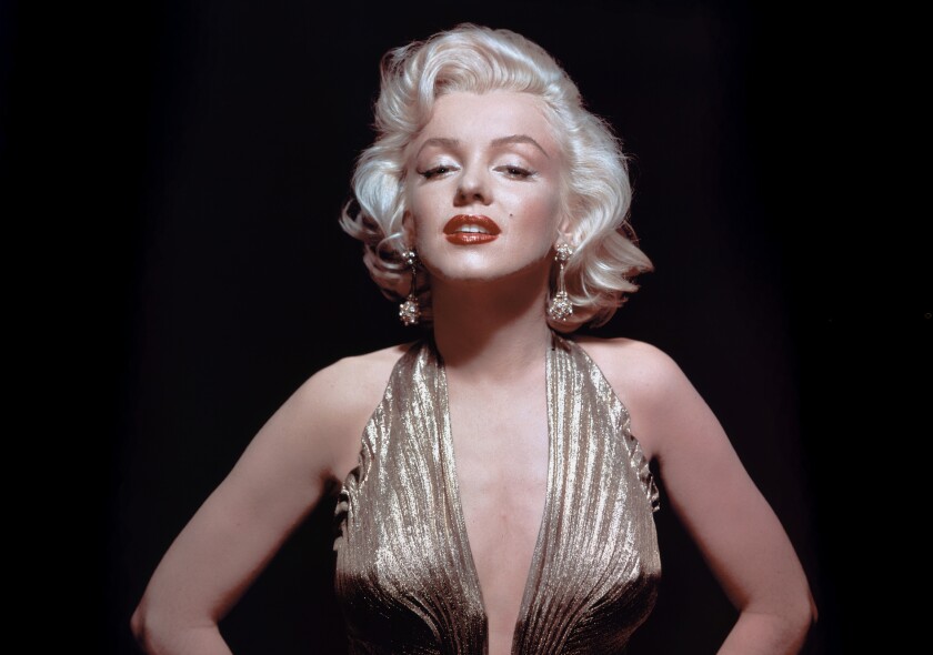 A platinum blonde Marilyn Monroe in a gold lame gown looks alluringly into the camera.