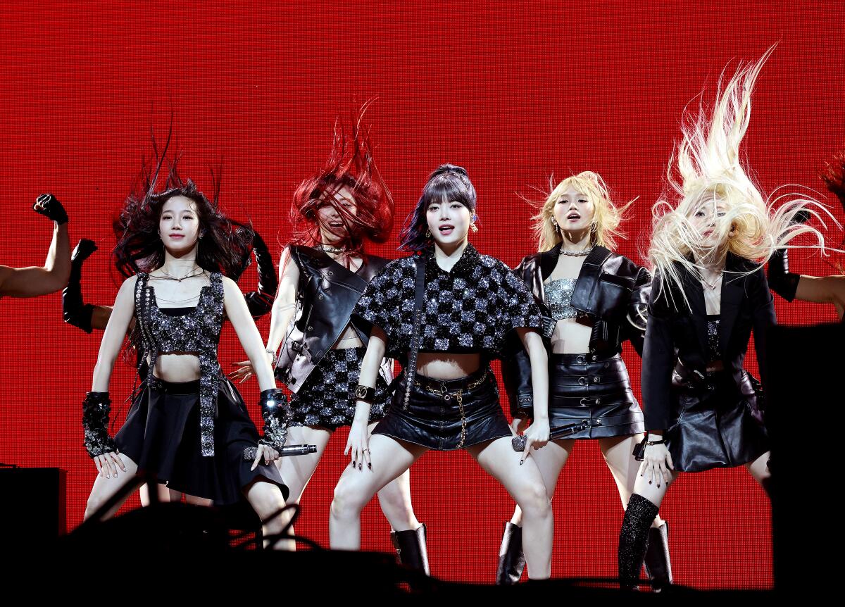 Women in black outfits dance while their long hair flies in front of a red background