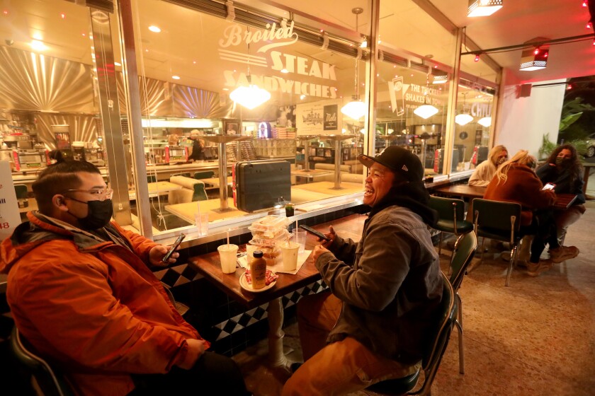 Couple eat outside as restaurant several feet from another table of people.