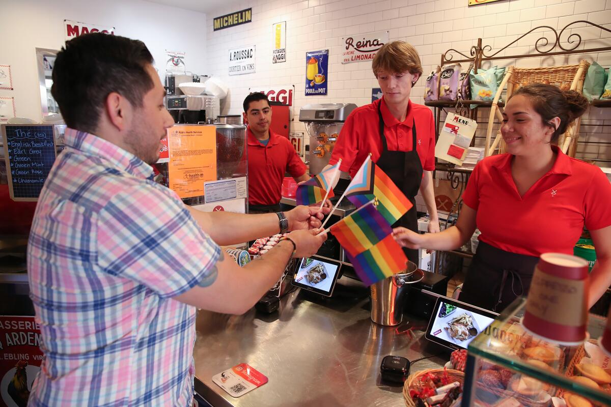 Volunteer coordinator Jonny Navarrete hands out Pride flags to workers at Moulin Cafe in downtown Laguna Beach.
