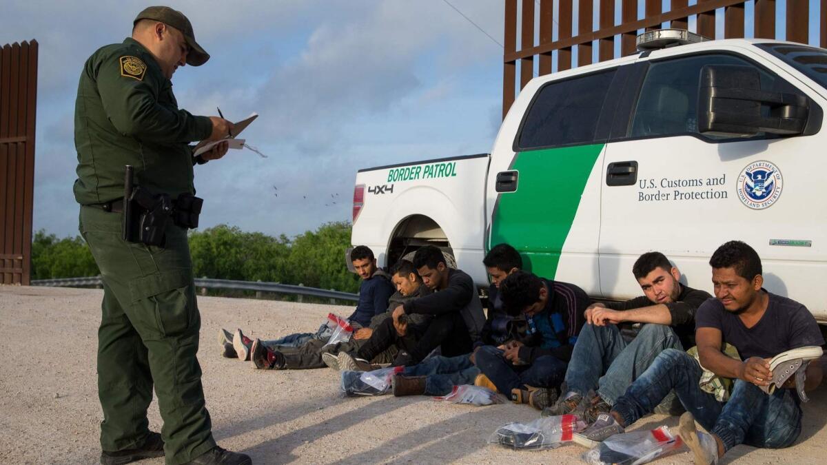 A Border Patrol agent apprehends immigrants shortly after they crossed the border from Mexico near McAllen, Texas, on March 26.