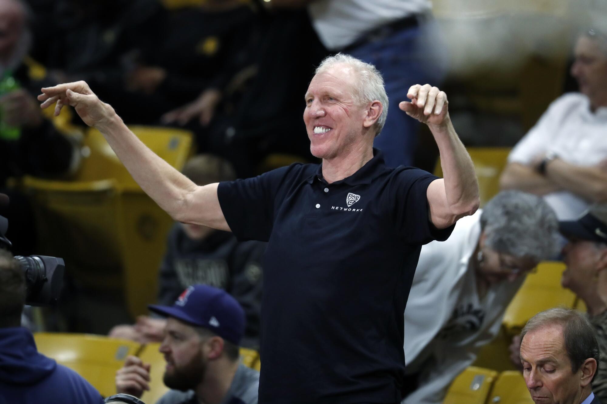Bill Walton smiles and raises his arms as he acknowledges fans at a Pac-12 basketball game