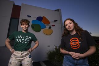 A woman wearing a green "Union Daddy" T-shirt poses in front of a building next to a woman wearing a black-and-orange T-shirt