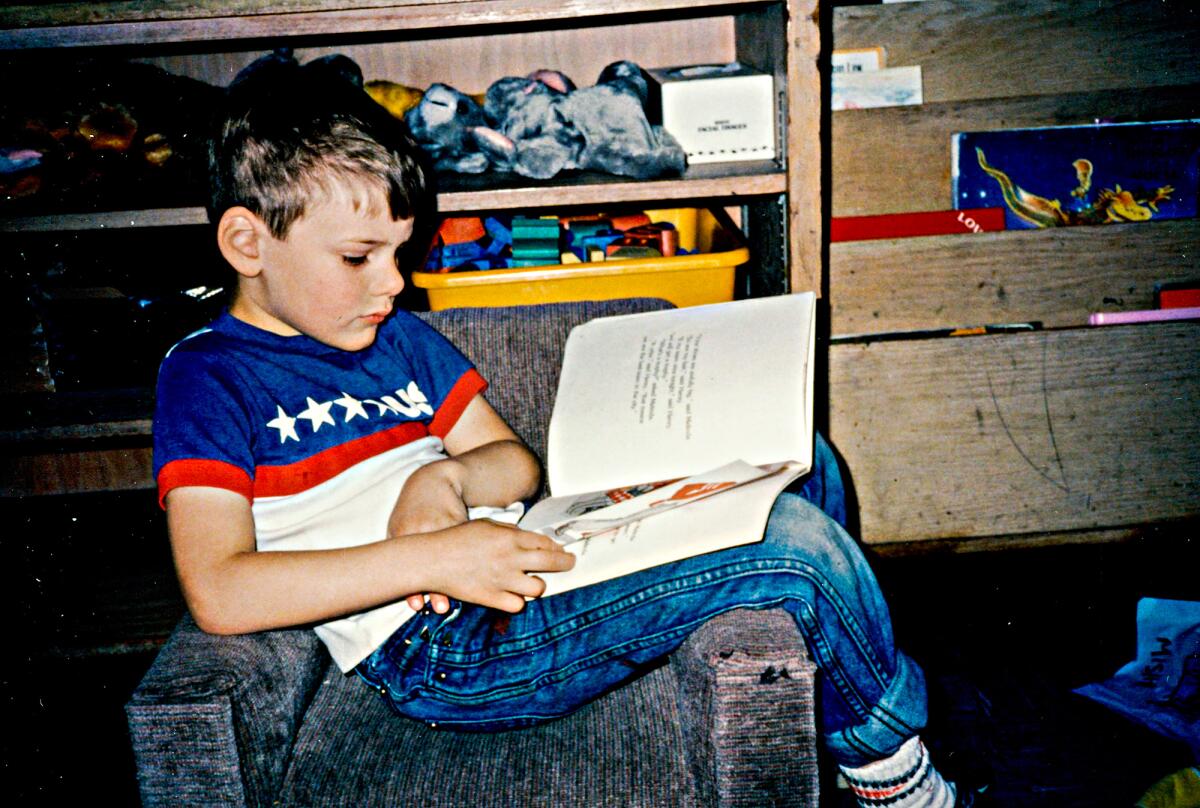 A boy reads sitting across a chair.