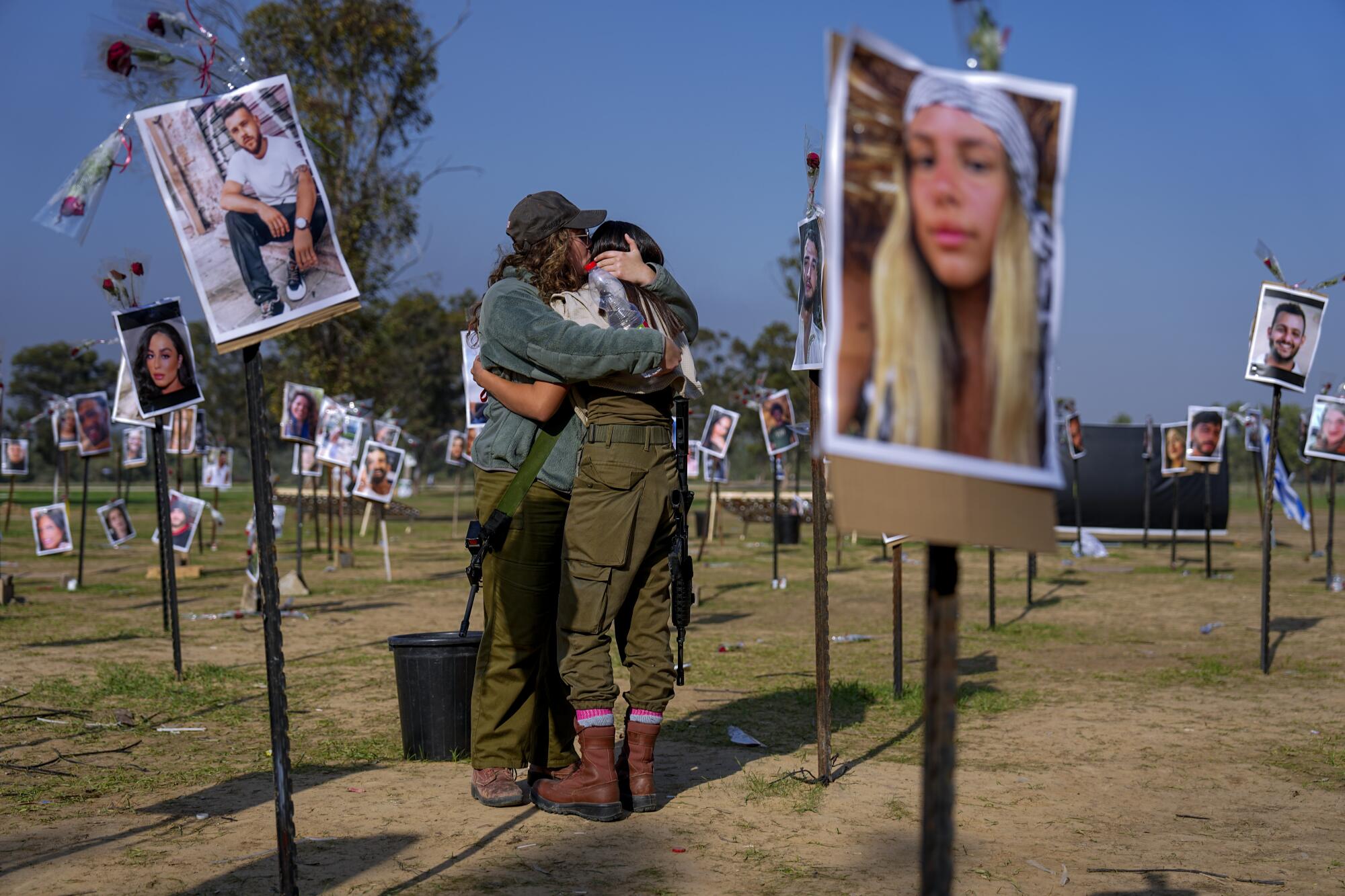 Israeli soldiers embracing next to photos of people killed or taken captive by Hamas