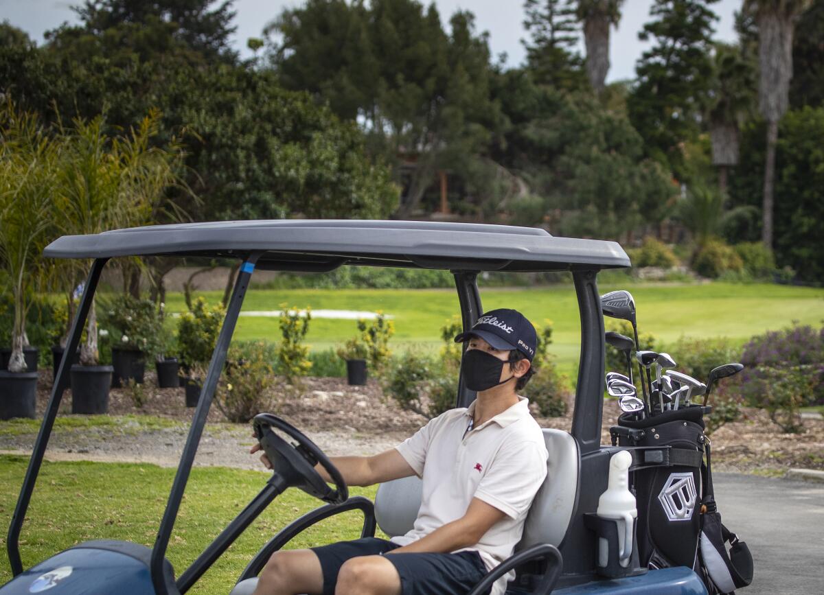 A golfer wears a protective mask while driving the golf cart