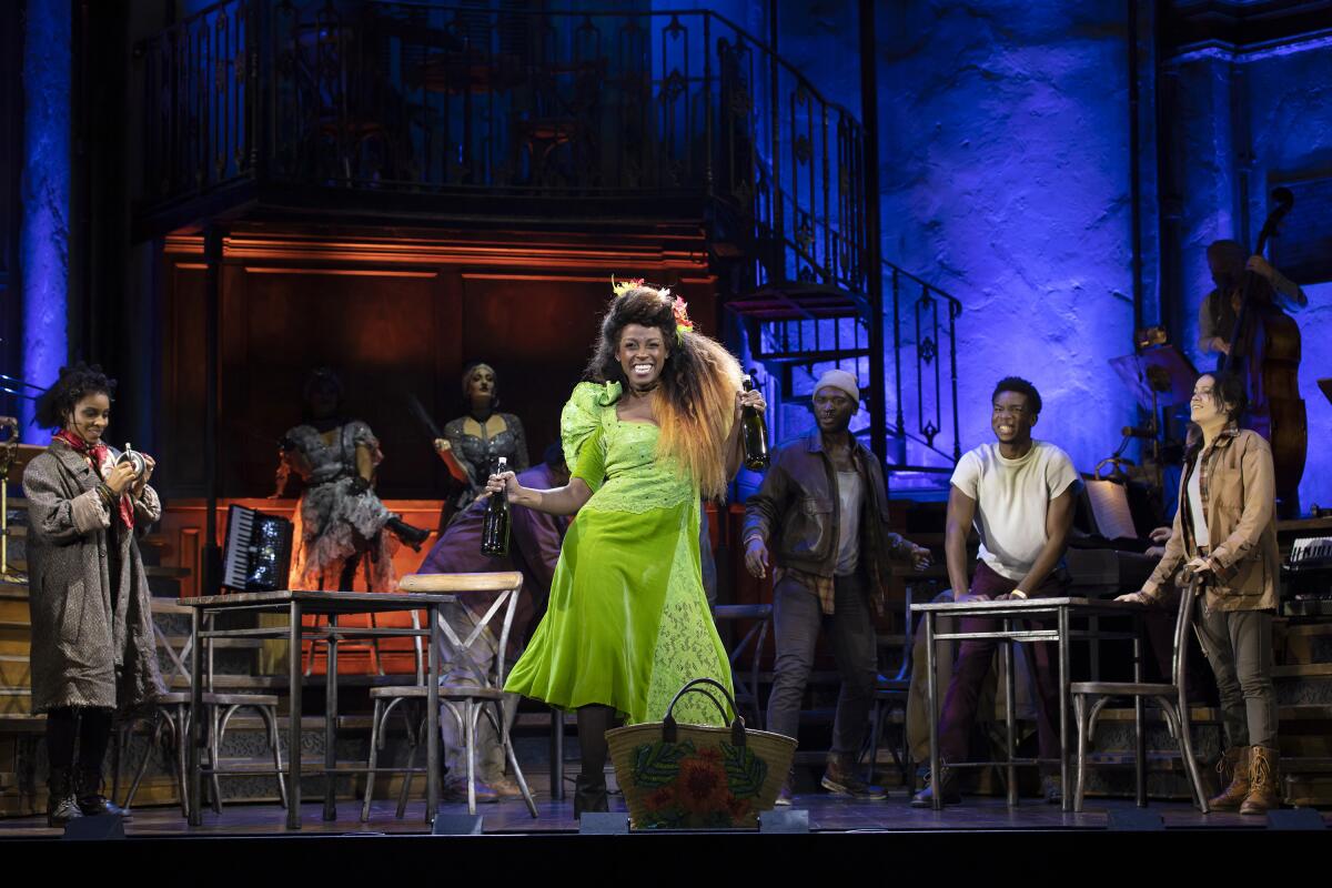 A woman in a green dress dances onstage as other actors watch from behind her. 